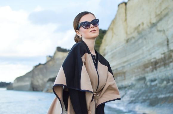 Outerwear - woman wearing black and brown dress and sunglasses standing near body of water under white and blue sky