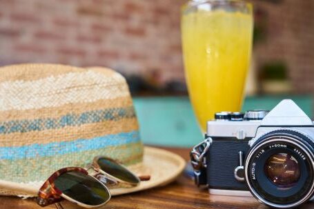 Stylish Vacation Essentials - Gray and Black Dslr Camera Beside Sun Hat and Sunglasses